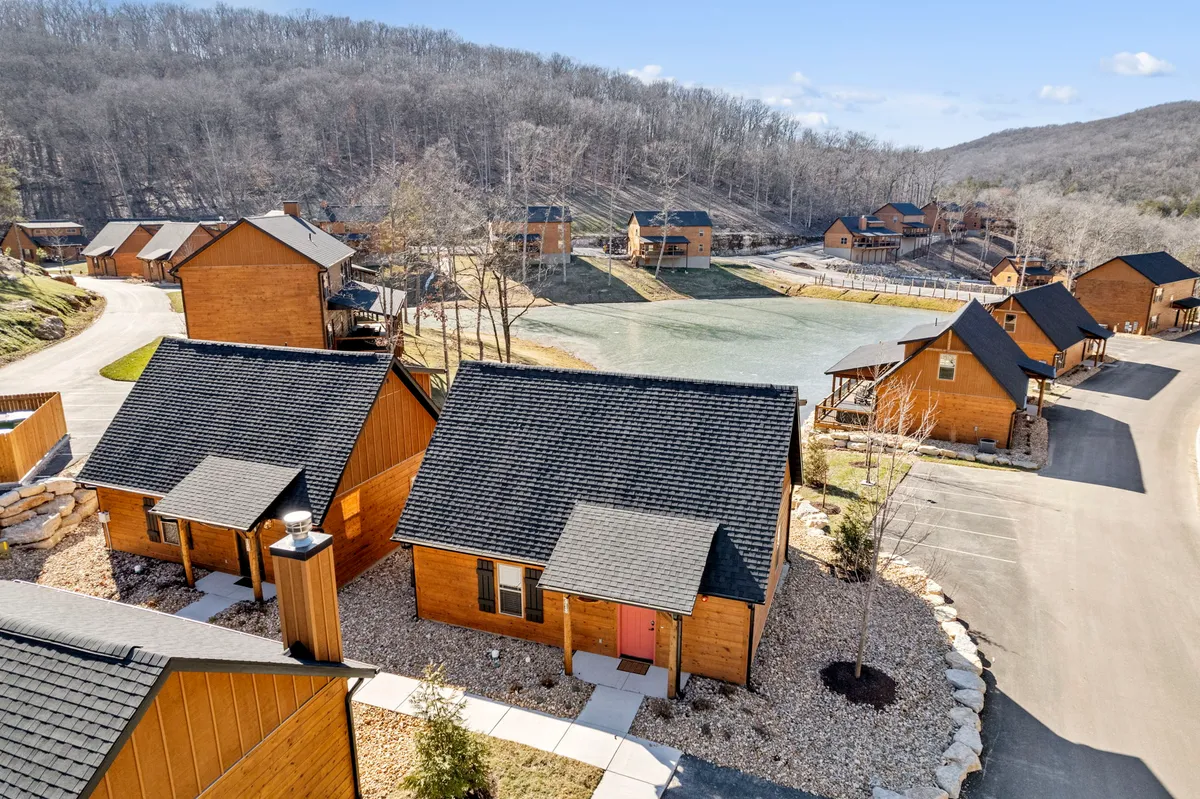 A tranquil lakeside scene featuring cozy wooden cabins nestled among trees, with a calm lake in the foreground. The natural setting exudes peace, scenic beauty, and seclusion, making it an ideal spot for couples to relax and reconnect.