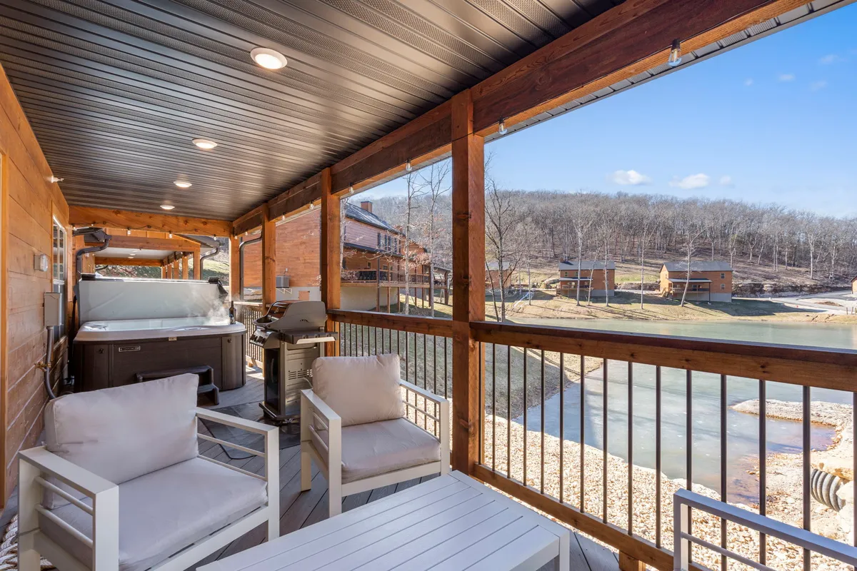 A spacious deck featuring a hot tub, outdoor seating, and a grill, with a serene scenic view in the background. The area is surrounded by lush greenery and offers a direct vantage point over the natural landscape.