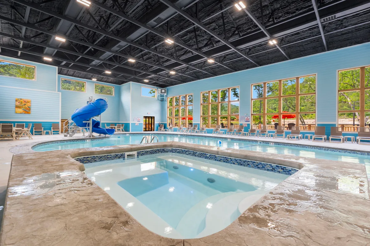 This interior image features an indoor pool with a water slide, jacuzzi, and large windows letting in natural light. Lounge chairs line the poolside, evoking a sense of relaxation and fun. The playful, family-friendly setting echoes the section’s mention of community amenities available for unwinding after a day outdoors.