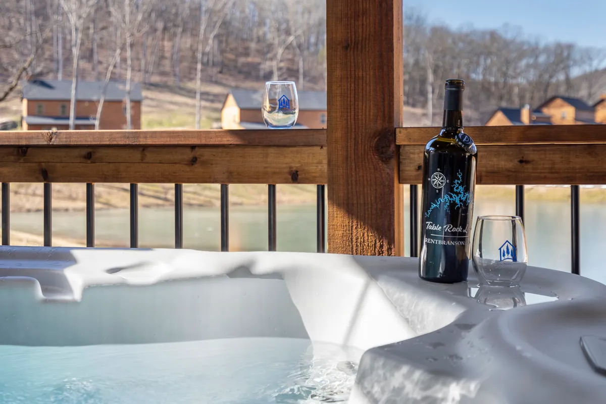 A luxurious hot tub set indoors with a bottle of wine and two glasses placed on the edge, all framed by a scenic view through large windows. Soft lighting and serene surroundings emphasize privacy and relaxation, evoking an intimate, romantic atmosphere.