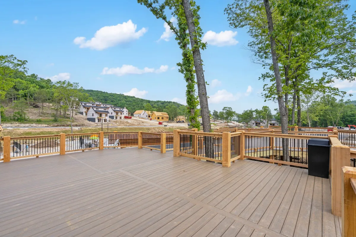 A wooden deck nestled among trees, with comfortable seating and a view of nearby houses, inviting relaxation and outdoor gatherings in a peaceful natural setting.