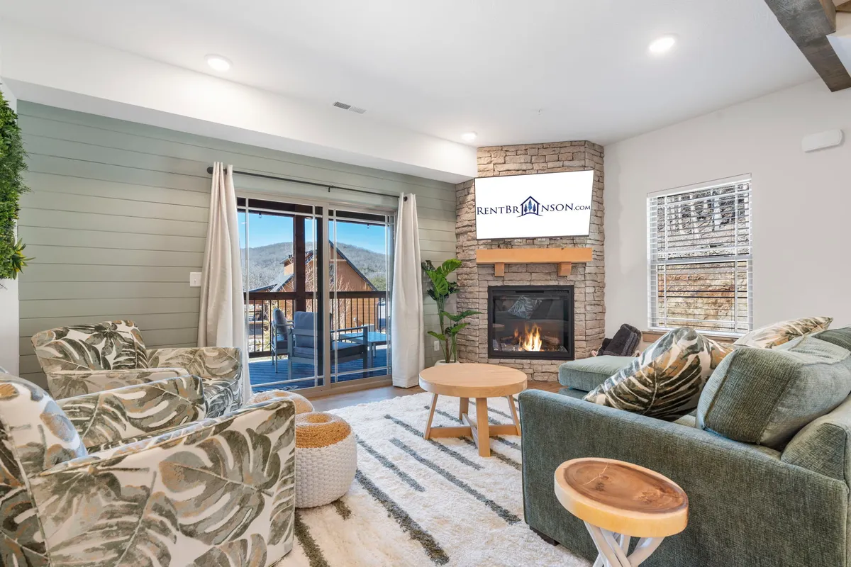 The image showcases a cozy cabin living room with a crackling fireplace, a plush sofa, and a coffee table set in front of expansive windows that reveal tranquil water views. The warm lighting and inviting decor create a relaxing, homey atmosphere perfect for unwinding after a day at Table Rock Lake.