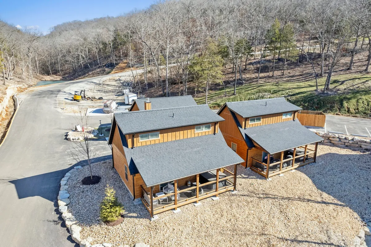 This exterior image features two inviting cabins nestled among trees, set against gravel landscaping. The scene suggests a peaceful, natural environment ideal for family gatherings, relaxing on porches, or embarking on nature walks. The soft evening light hints at the promise of sunset views and cozy evenings by the fire pit, while the surrounding greenery connects directly to the adventure and exploration narrative.