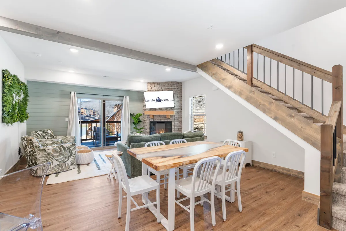 A view from the dining area that highlights a green couch, a fireplace, a spacious dining table, and large windows that let in abundant sunlight. The space feels both cozy and vibrant, encouraging shared meals and laughter around the table.