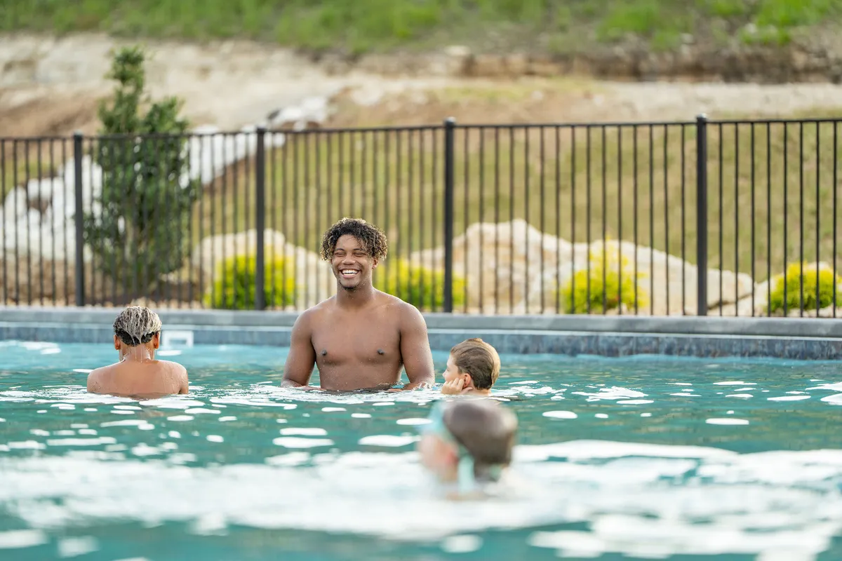 Children play joyfully in a clear swimming pool, with a smiling boy in focus. The scene emphasizes carefree fun, laughter, and bonding through water games—perfectly reflecting the year-round indoor and seasonal outdoor pool access offered at the resort.